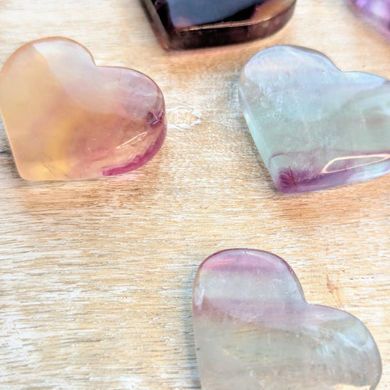 Heart-shaped rainbow fluorite stones in various colors on a wooden surface