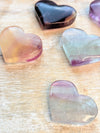 Heart-shaped rainbow fluorite stones in various colors on a wooden surface