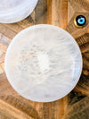 A round white stone bowl with a cloudy, marbled texture, photographed from above on a rustic wooden surface.