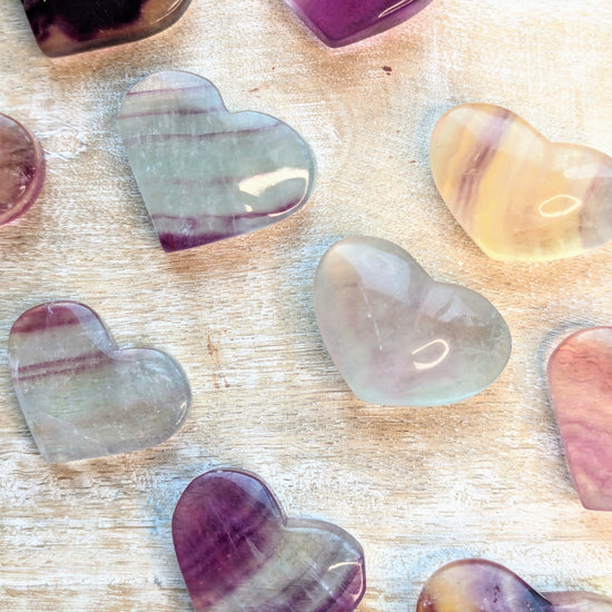 Heart-shaped rainbow fluorite stones in various colors on a wooden surface