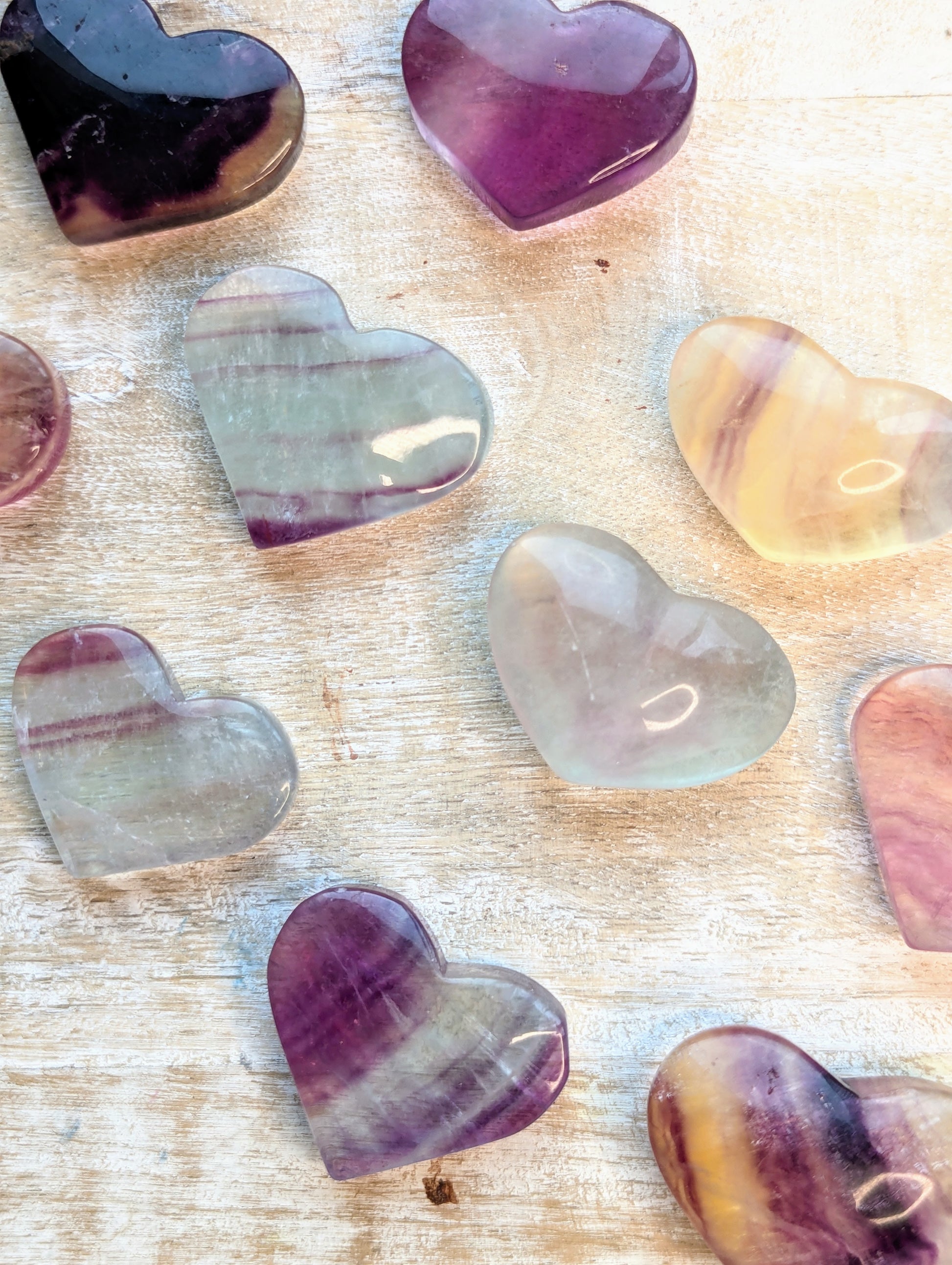 Heart-shaped rainbow fluorite stones in various colors on a wooden surface