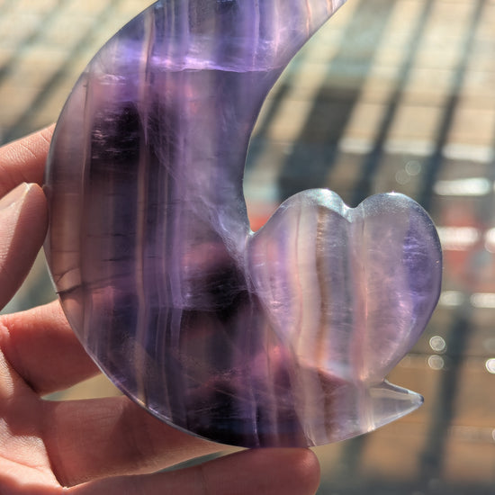 Hand holding a purple crystal heart-shaped object with a blurred background