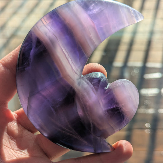 Hand holding a purple and white semi-precious stone with a blurred background