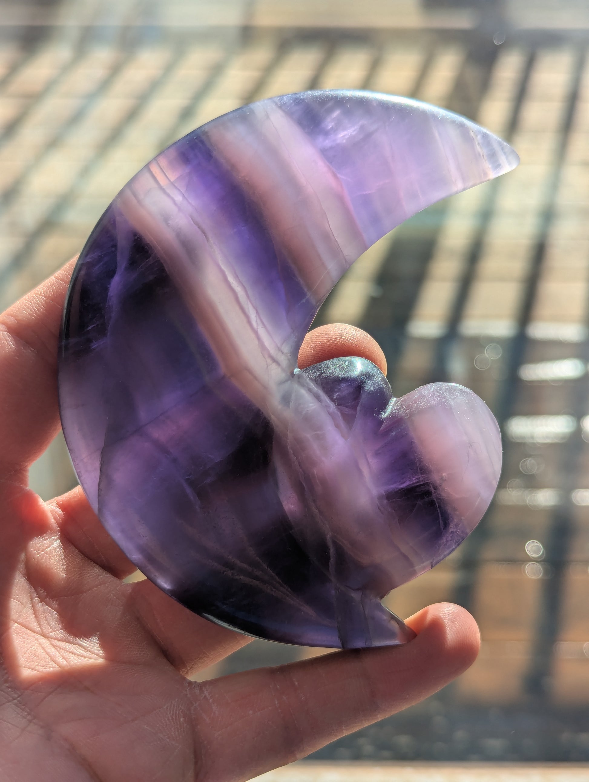 Hand holding a purple and white semi-precious stone with a blurred background