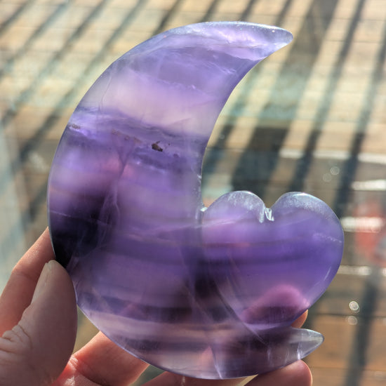 Hand holding a purple and clear crystal with a blurred background